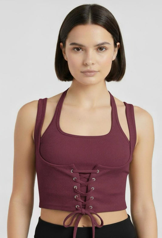 Close-up of a female model wearing a fitted burgundy (or maroon/wine) ribbed halter crop top with a corset-style lace-up front and a tie at the hem.