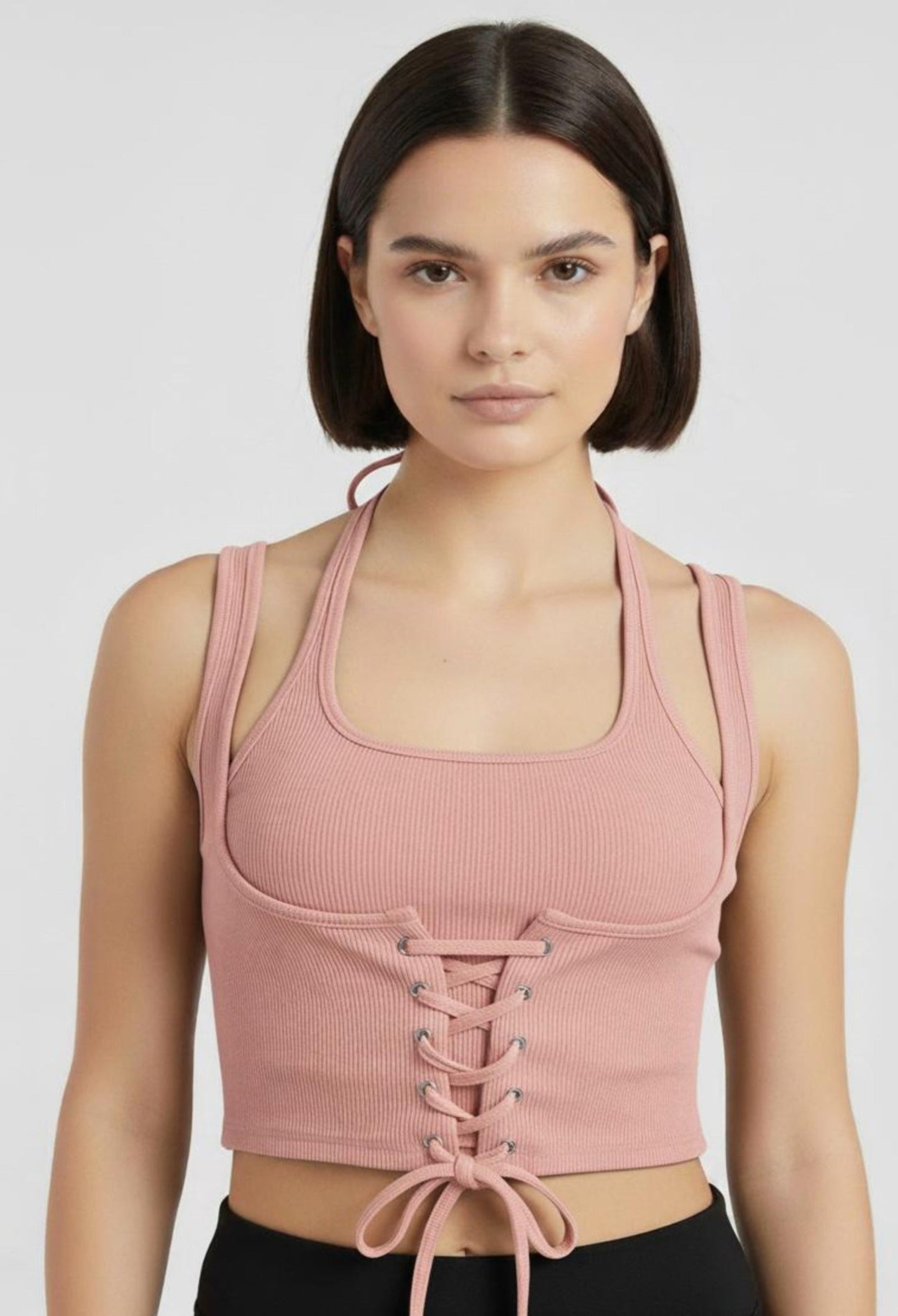 Close-up of a female model wearing a fitted peachy ribbed halter crop top with a corset-style lace-up front and a tie at the hem.