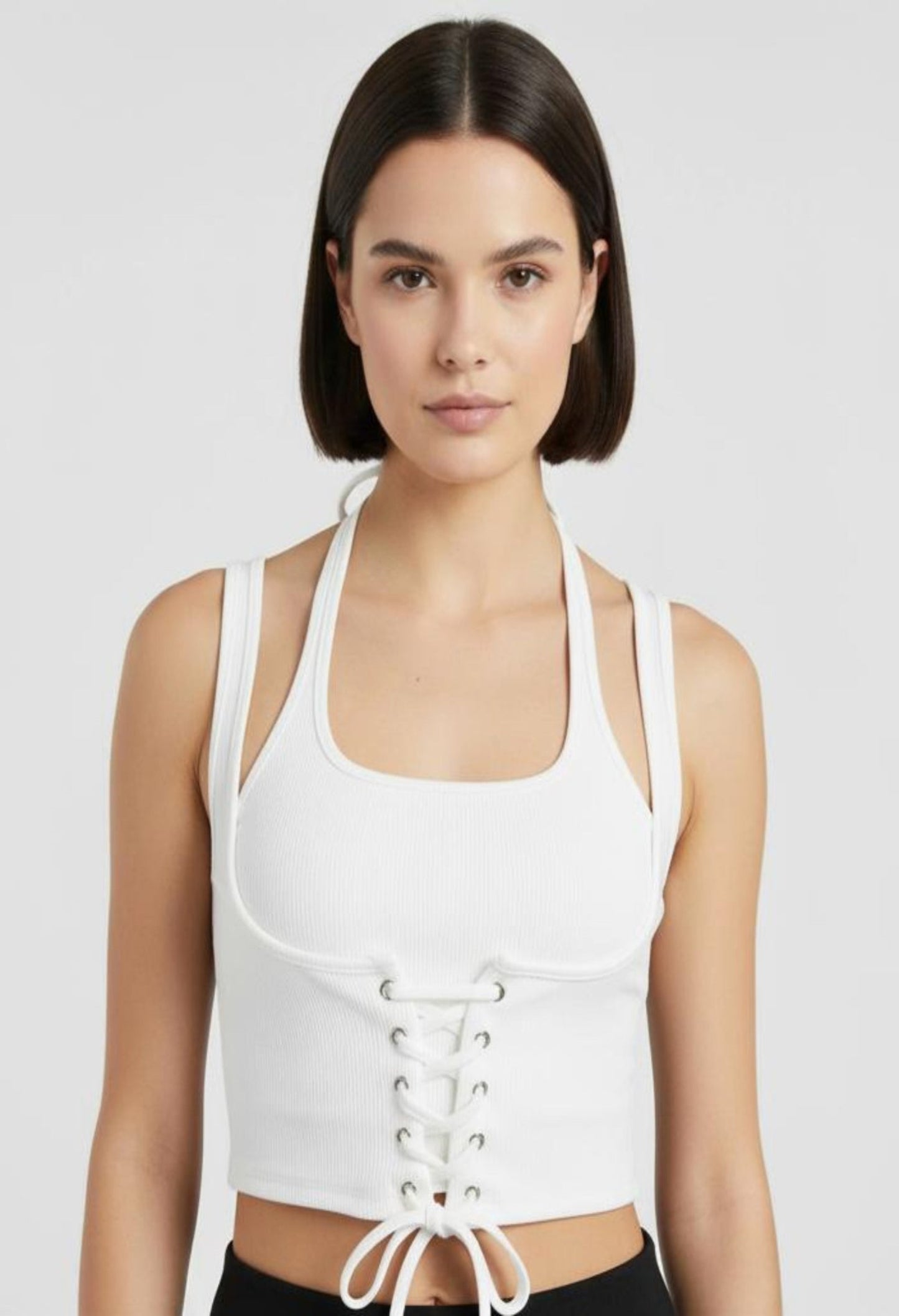 Close-up of a female model wearing a fitted white ribbed halter crop top with a corset-style lace-up front and a tie at the hem.