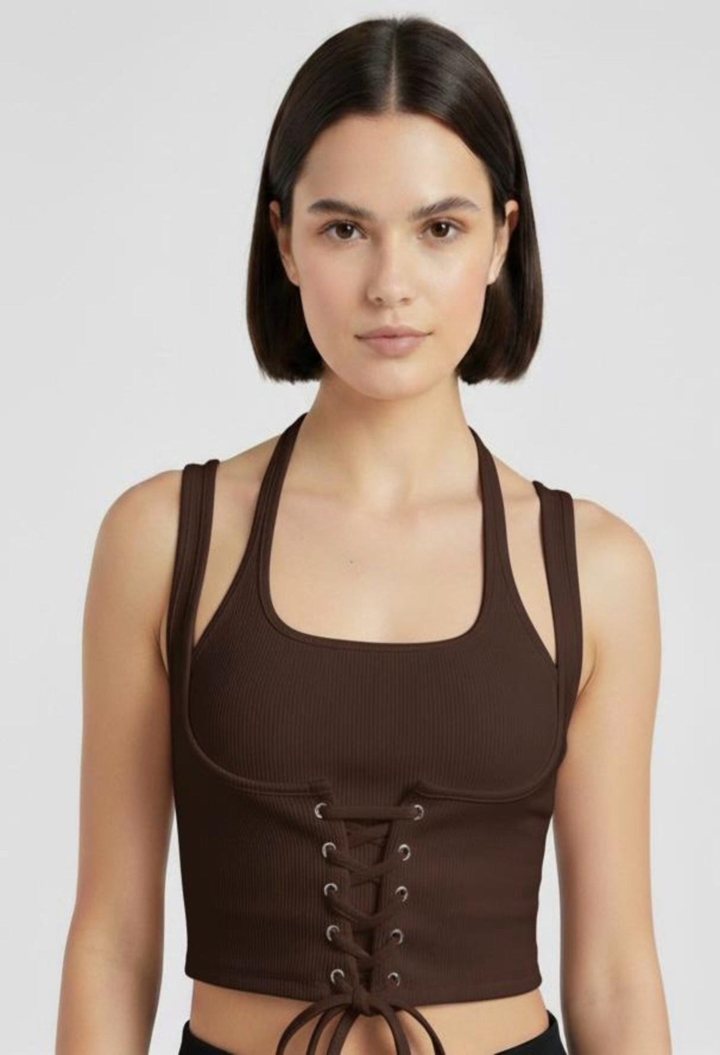 Close-up of a female model wearing a fitted brown ribbed halter crop top with a corset-style lace-up front and a tie at the hem.
