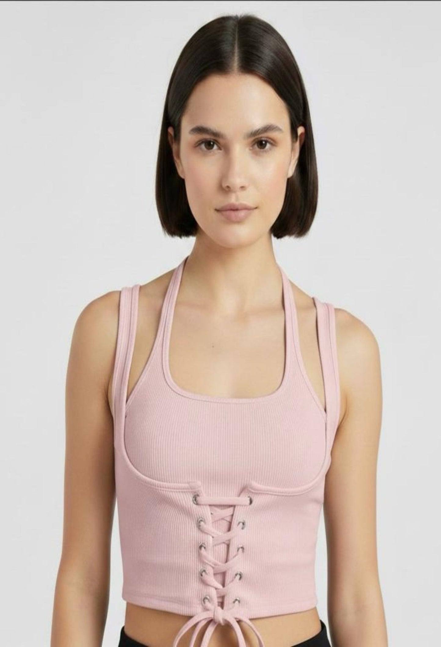 Close-up of a female model wearing a fitted pink ribbed halter crop top with a corset-style lace-up front and a tie at the hem.