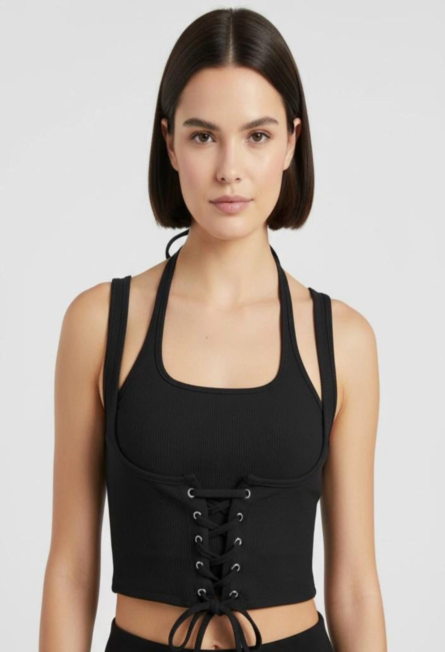 Close-up of a female model wearing a fitted black ribbed halter crop top with a corset-style lace-up front and a tie at the hem.